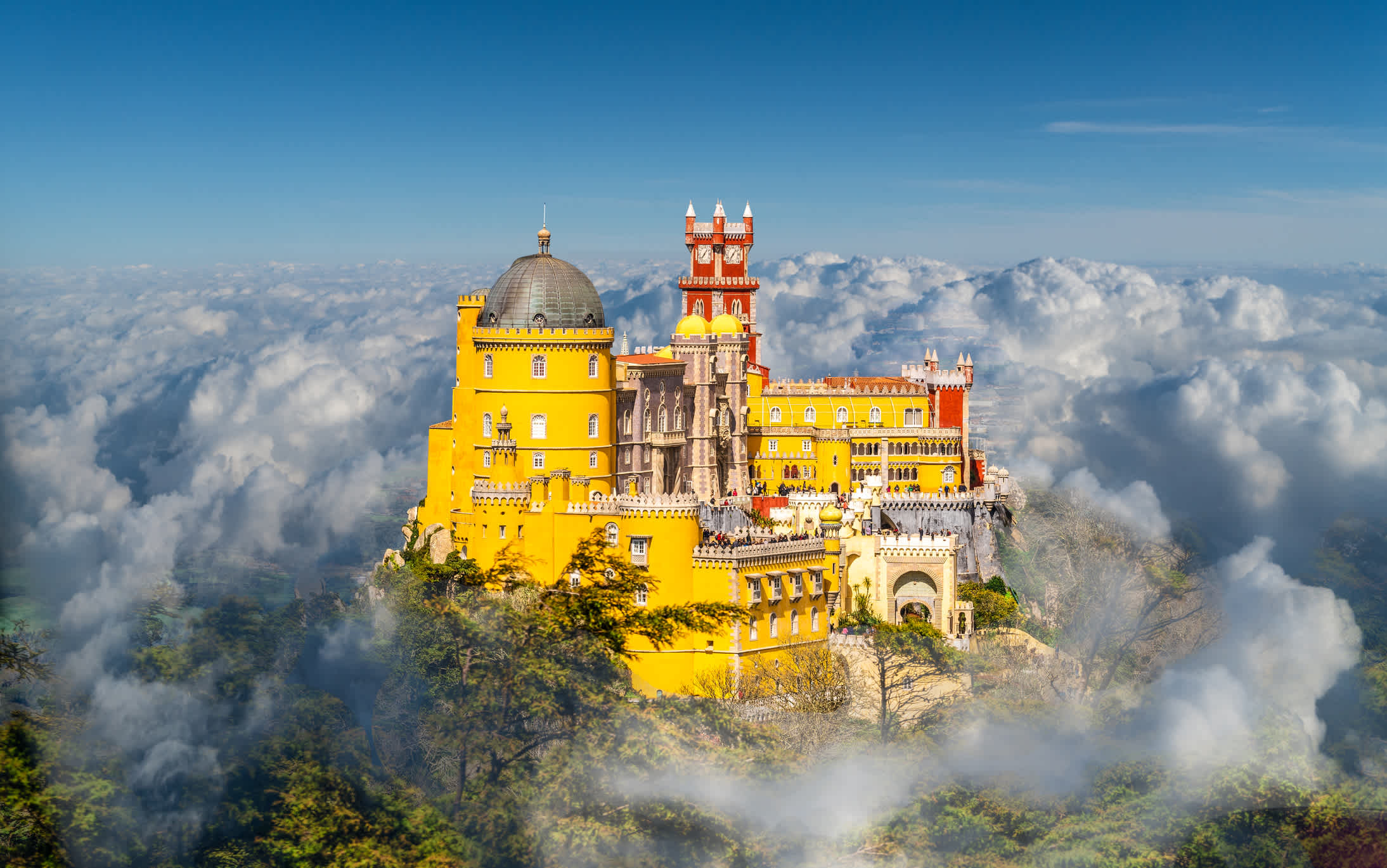 Château jaune et rouge trônant au sommet d'une colline dans les nuages, à Sintra, au Portugal.