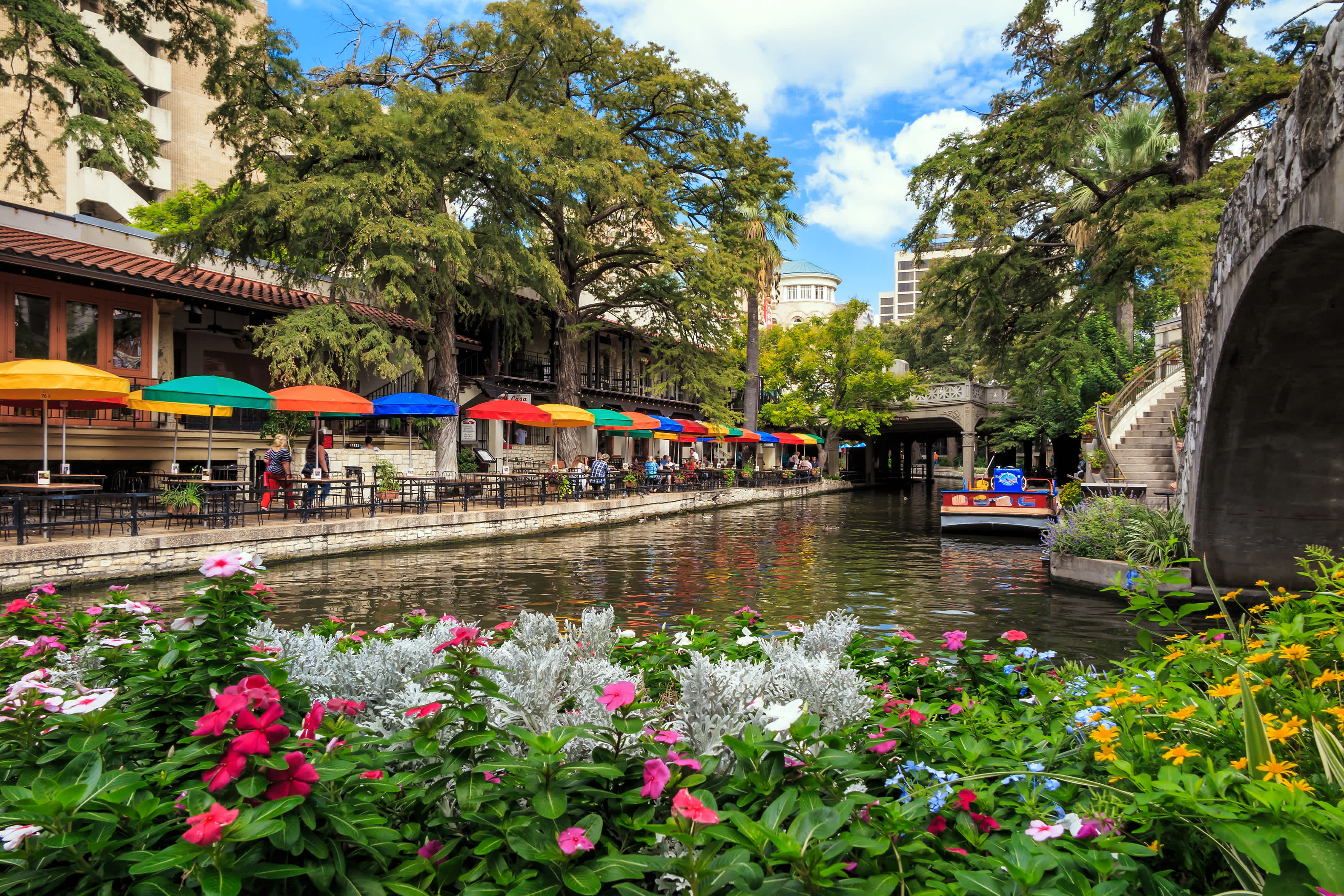 Fleurs aménagés le long d'un canal à San Antonio, avec des tables et des parasols colorés le long de la rive.