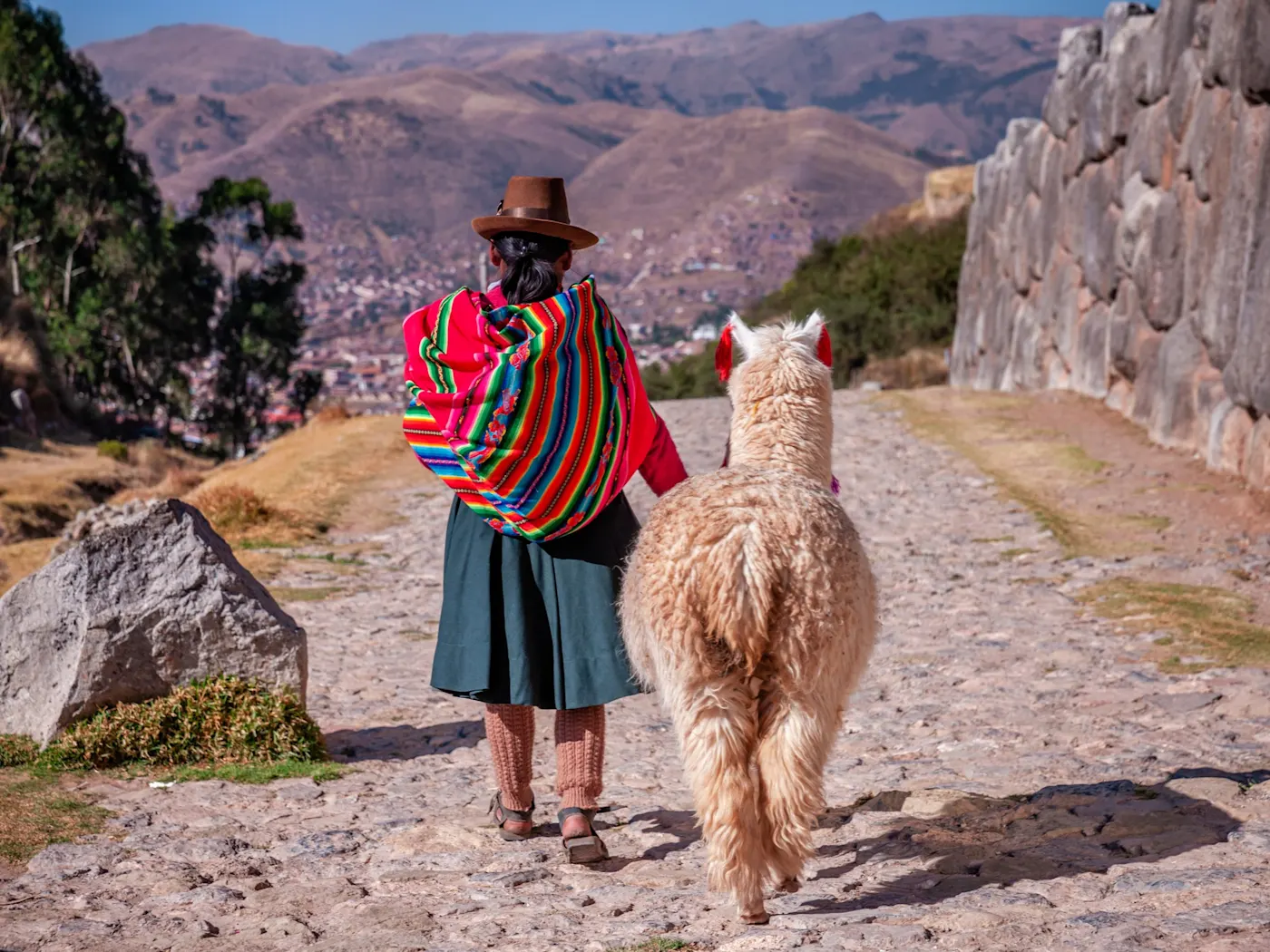 Cusco, Peru Frau in traditioneller Kleidung mit Alpaka auf steinernem Weg, Blick auf Cusco, Cusco, Peru.