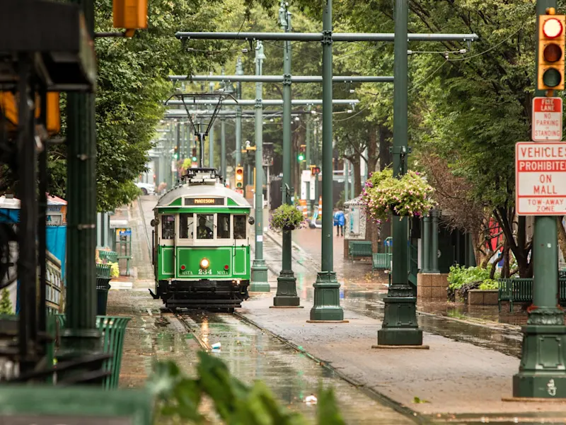 Memphis, Tennessee, USA Historische grüne Straßenbahn auf einer regennassen Straße mit Bäumen und Blumen. Memphis, Tennessee, USA.