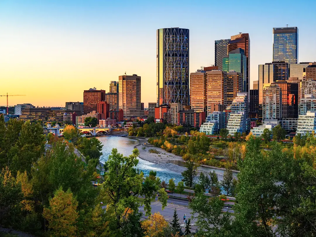 Skyline von Calgary bei Sonnenuntergang mit Fluss und Brücke im Vordergrund, Alberta, Kanada.