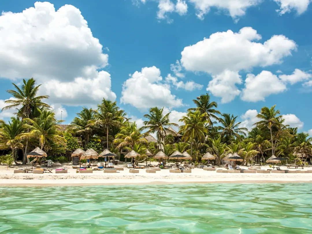 Tropischer Sandstrand mit Palmen, strohgedeckten Sonnenschirmen und türkisfarbenem Meer. Tulum, Quintana Roo, Mexiko

