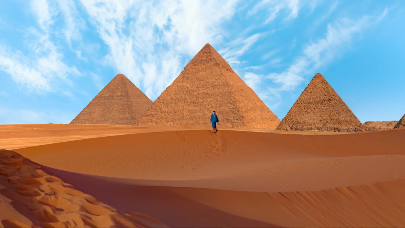 Eine kleine menschliche Figur ist am Boden vor den Pyramiden zu sehen.  Gizeh, Kairo, Ägypten, 