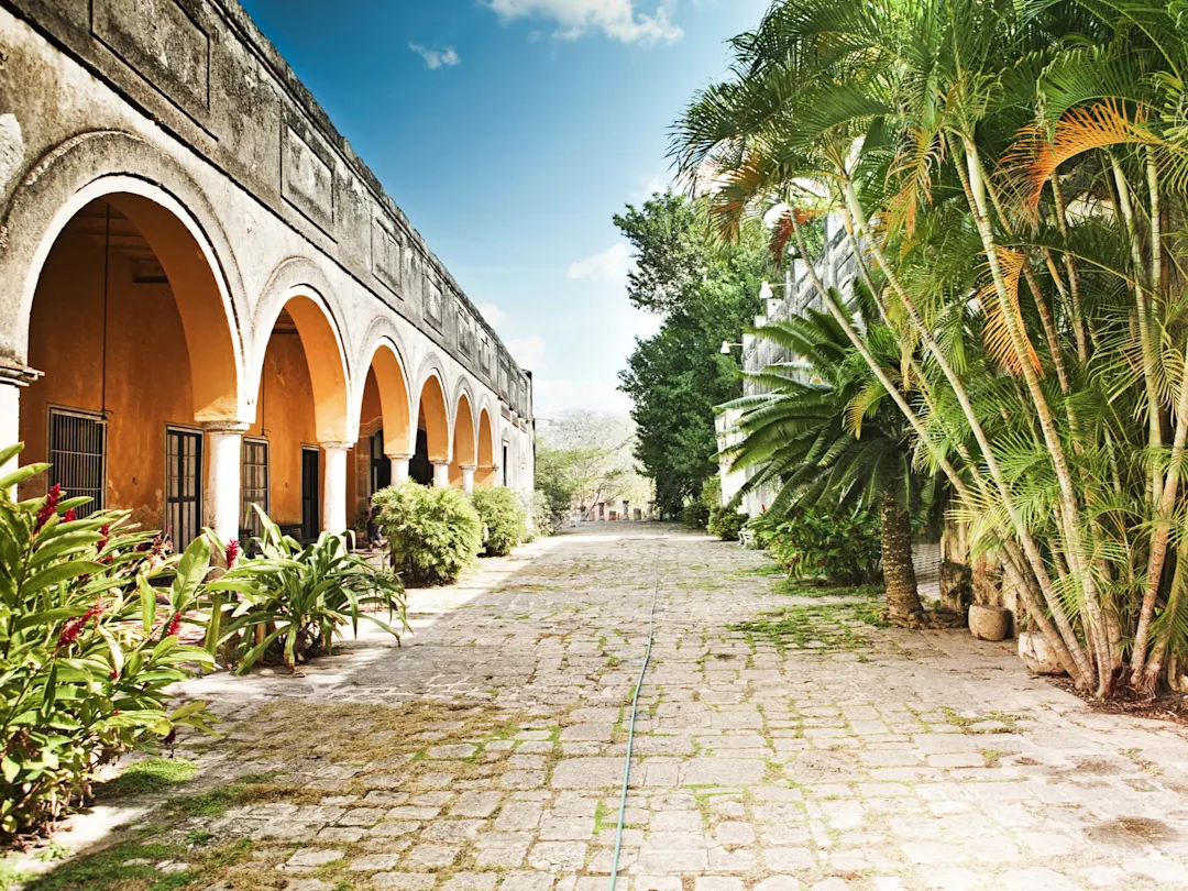 Helle Kolonialarchitektur mit Bögen und tropischen Pflanzen im Innenhof. Mérida, Yucatán, Mexiko.