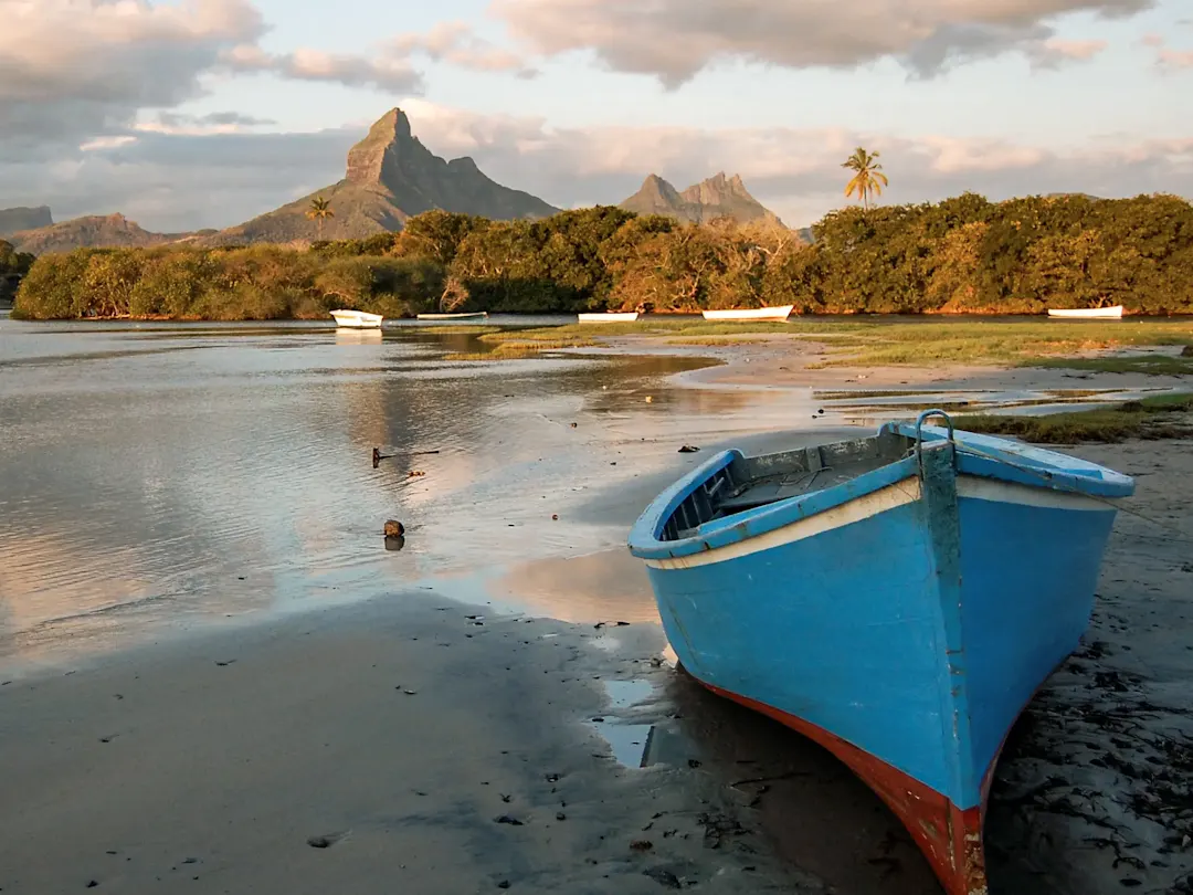 Blaues Fischerboot am Ufer mit Bergen im Hintergrund, Tamarin, Mauritius.