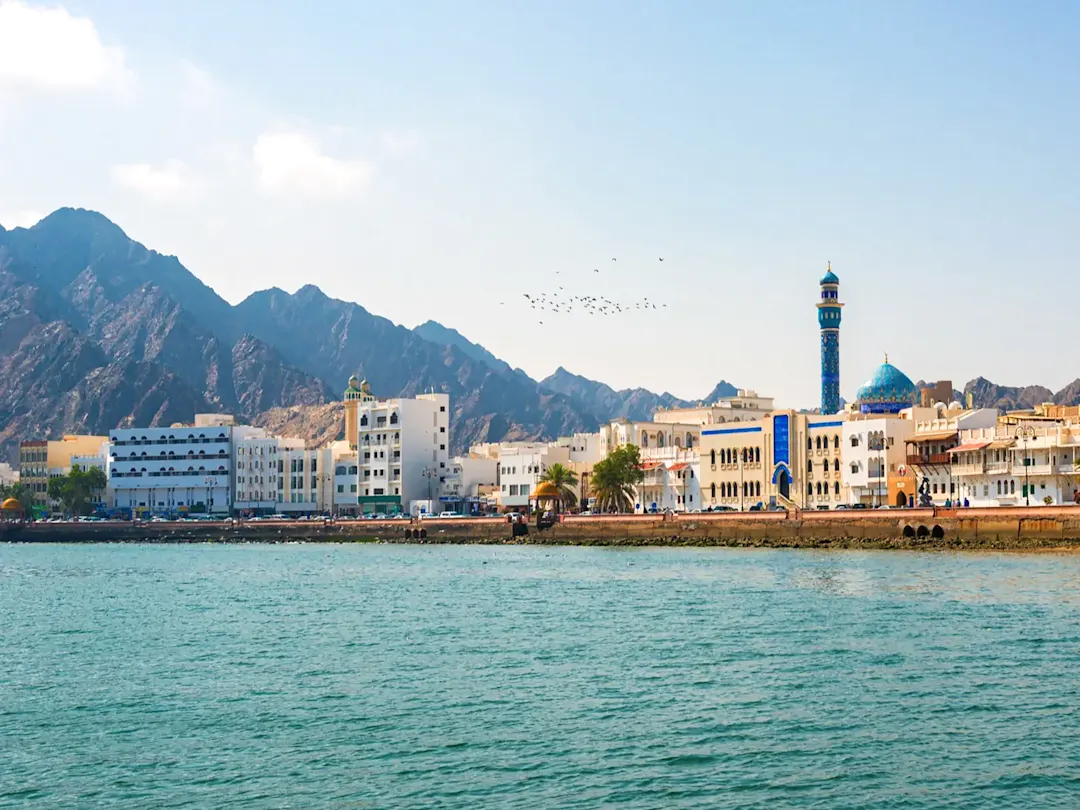 Weiße Gebäude an der Corniche mit Bergen im Hintergrund. Mutrah, Muscat, Oman.
