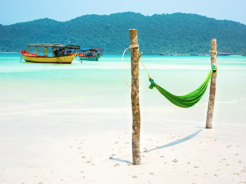 Koh Rong Samloem, Kambodscha Grüne Hängematte am weißen Sandstrand mit Fischerbooten im türkisfarbenen Wasser. Koh Rong Samloem, Kambodscha.