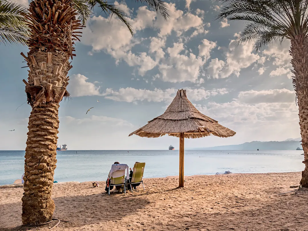 Sandstrand mit Strohdach, Palmen und Blick auf das Rote Meer. Yanbu, Medina, Saudi-Arabien.
