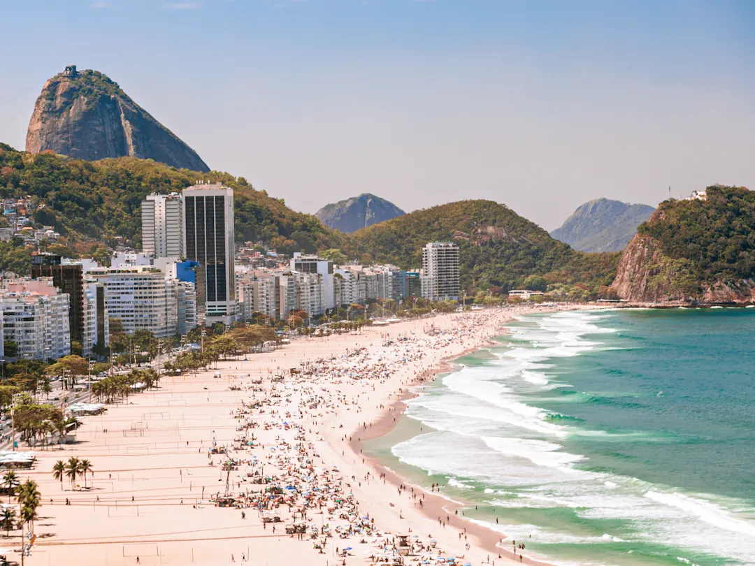 Lebhafter Sandstrand mit Stadt und Bergen im Hintergrund, Copacabana, Rio de Janeiro, Brasilien.