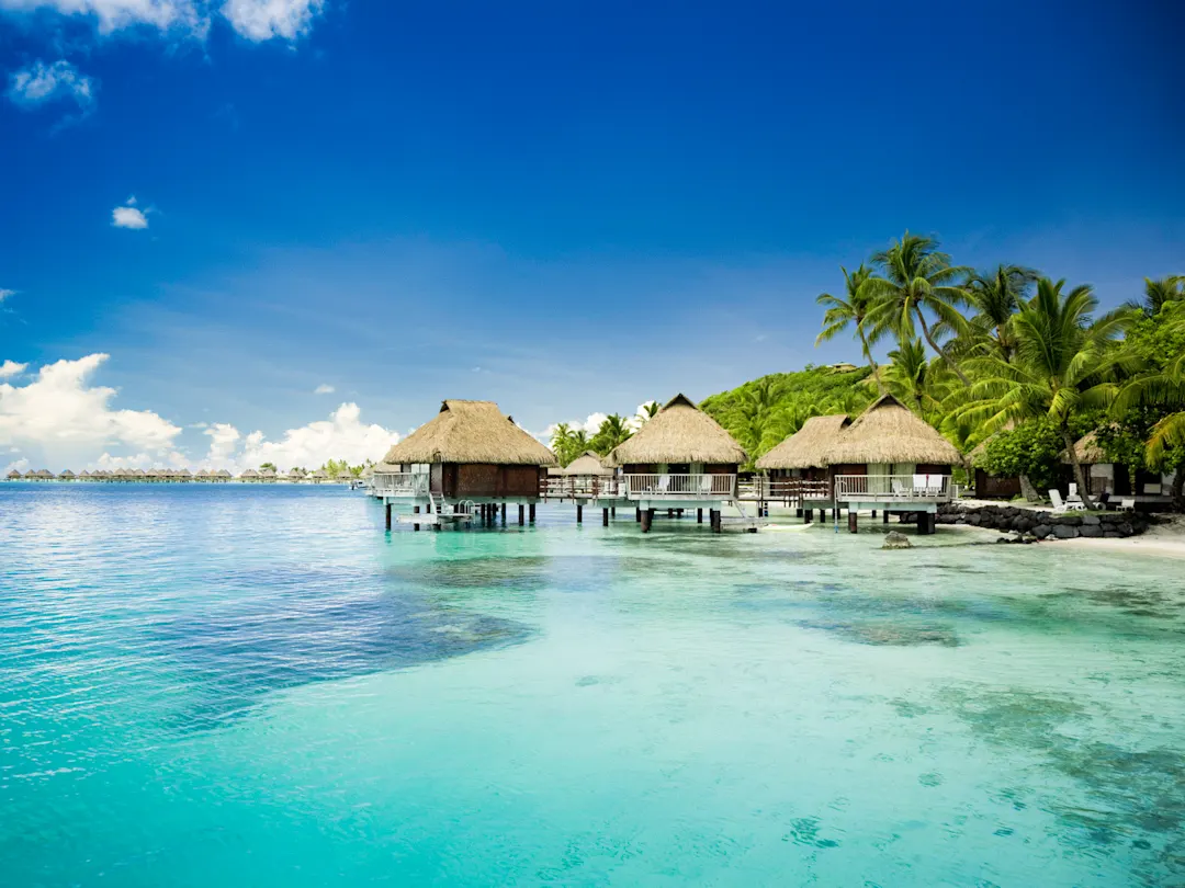 Wasserbungalows auf Stelzen im türkisfarbenen Meer vor einer tropischen Insel. Tahiti, Französisch-Polynesien.