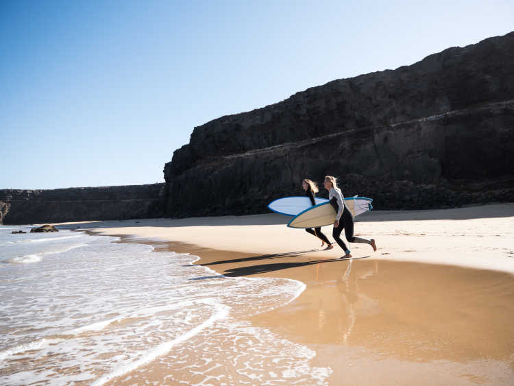 Zwei Surferin, die mit ihren Bretten auf das Meer zulaufen