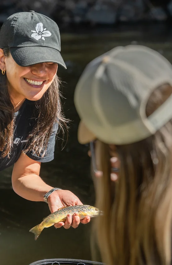 Woman in a hat smiling while holding a small fish