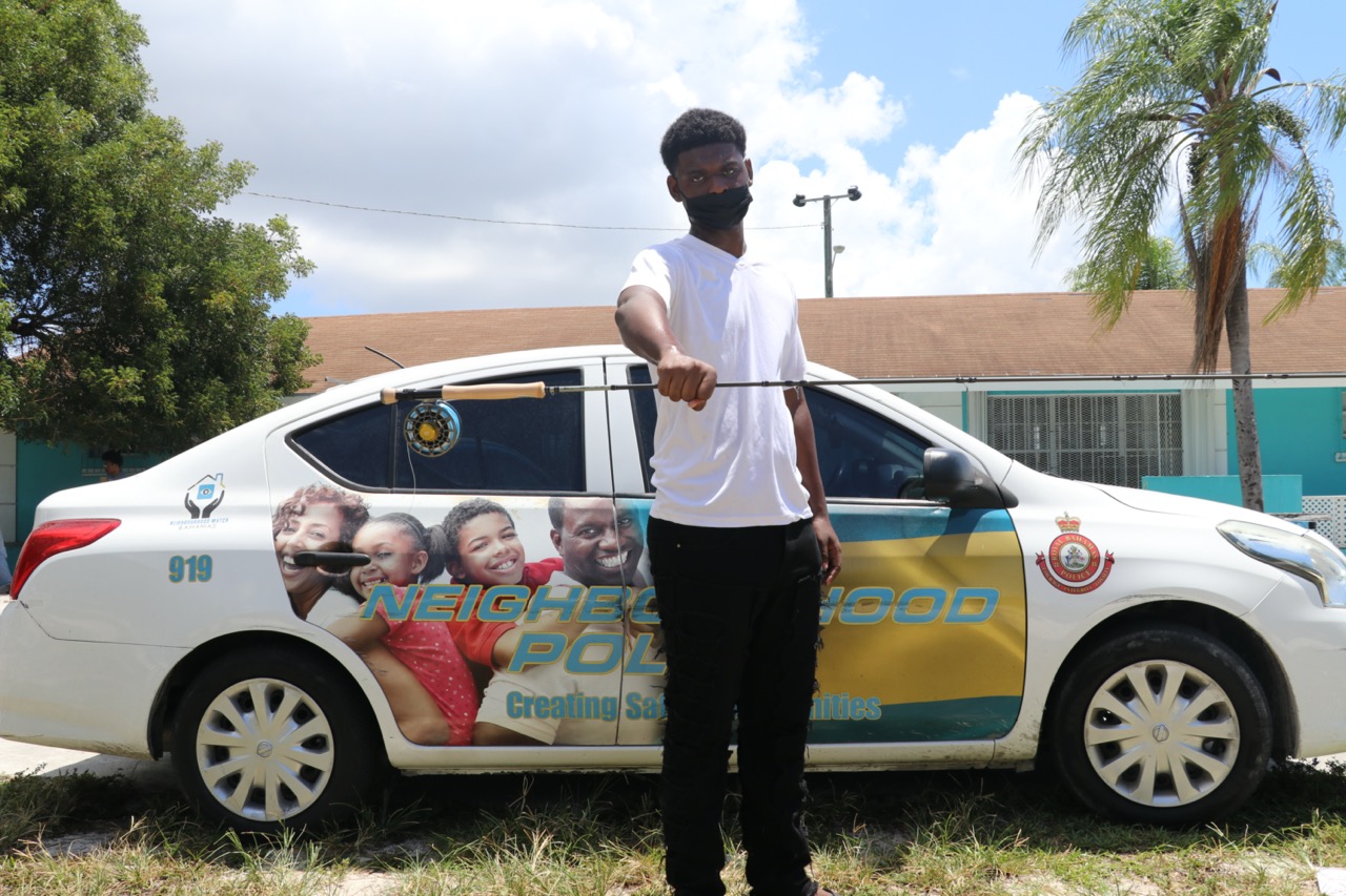 Man holding out a fly fishing rod in front of a car