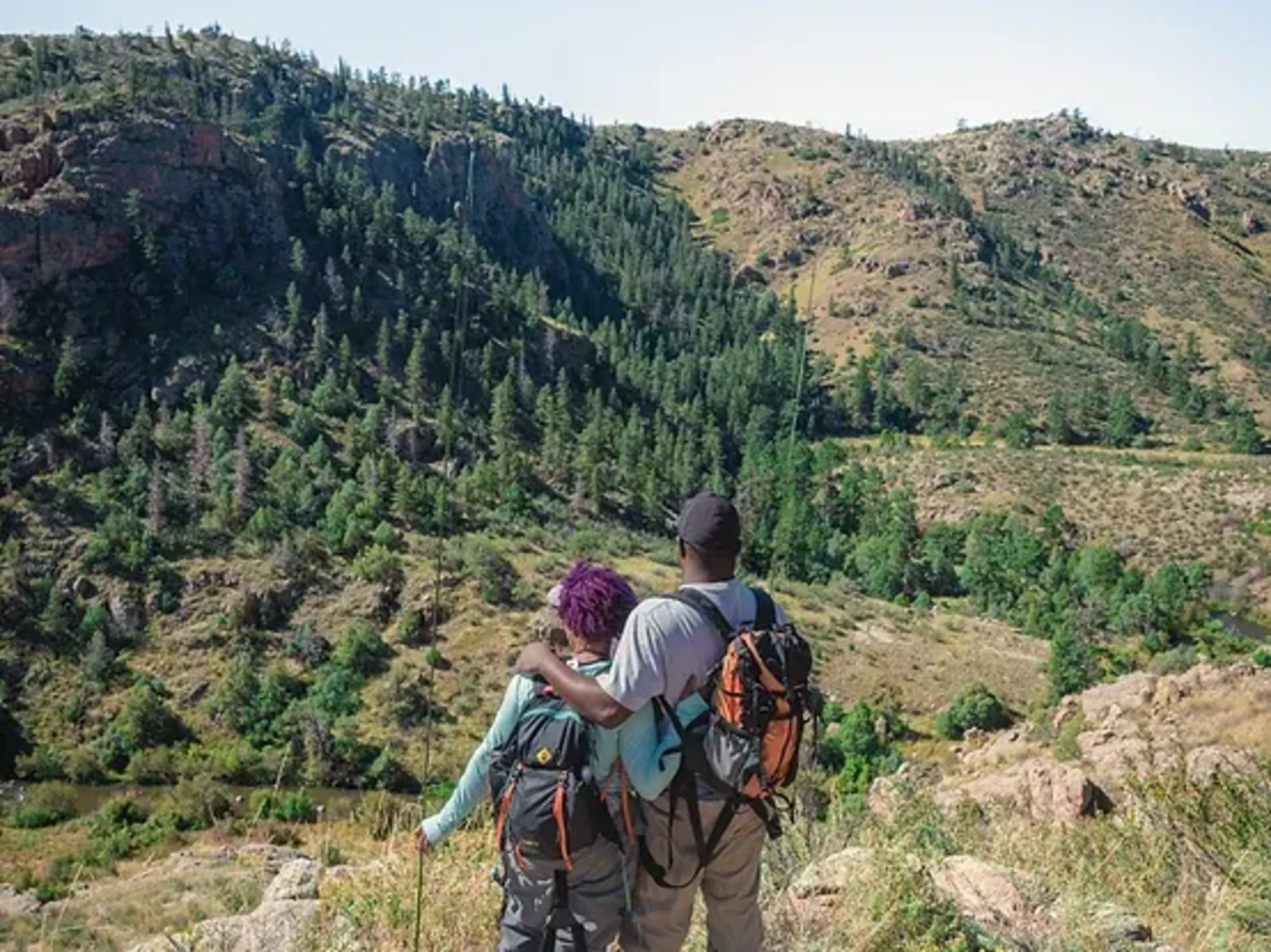Two people with backpacks hiking, with one person's arm around the other