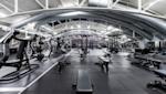 Moderne treningsstudio med svart treningsutstyr, store ventilasjonsrør i taket og hvite bjelker i industrielt design.