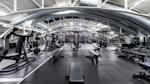 Moderne treningsstudio med svart treningsutstyr, store ventilasjonsrør i taket og hvite bjelker i industrielt design.