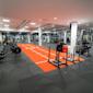 Modernt gym med orange träningsyta, roddmaskiner, viktställ och hantlar under rosa belysning i industriell lokal.