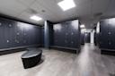 Moderne garderobe med mørke grå skap langs veggene, svarte benker og søyle i midten, hvitt tak med LED-lys.