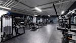 Moderne treningsstudio med svart treningsutstyr, grått gulv og eksponert hvitt tak med industriell belysning.