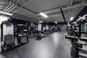 Moderne treningsstudio med svart treningsutstyr, grått gulv og eksponert hvitt tak med industriell belysning.