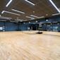 Rymligt träningsstudio med ljust trägolv, blå väggar, stora speglar och moderna LED-lampor i taket.