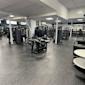 Modernt gym med svarta träningsapparater, vita pelare och grått golv under takbelysning.