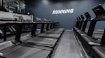 Moderne treningsstudio med rekker av svarte tredemøller og ordet RUNNING på blå vegg i bakgrunnen.