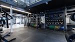 Moderne treningsstudio med mørke farger, LED-belysning, squat-stativer og organisert utstyr som vekter og plater.