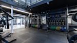 Moderne treningsstudio med mørke farger, LED-belysning, squat-stativer og organisert utstyr som vekter og plater.