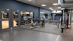 Modernt gym med blå väggar, grått golv, träningsutrustning och glasdörrar märkta Group Training Studio och Entrance.