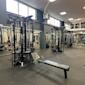 Modernt gym med svarta träningsstationer och kabelmaskiner, grått golv och stora fönster som släpper in naturligt ljus.