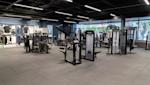 Modernt gym med svarta träningsredskap, grått golv, svart tak med LED-belysning och stora fönster i bakgrunden.