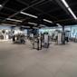 Modernt gym med svarta träningsredskap, grått golv, svart tak med LED-belysning och stora fönster i bakgrunden.