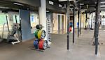 Modernt gym med viktställ, färgglada viktskivor och träningsutrustning under lysrör i svart tak.