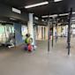 Modernt gym med viktställ, färgglada viktskivor och träningsutrustning under lysrör i svart tak.