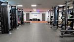 Modernt gym med styrketräningsutrustning, bänkpressar och vikter. Texten "PERFORMANCE ZONE" på väggen.