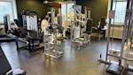 Modernt gym med vita och svarta träningsredskap, gröna väggar och exponerade ventilationsrör i taket.