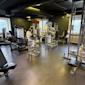 Modernt gym med vita och svarta träningsredskap, gröna väggar och exponerade ventilationsrör i taket.