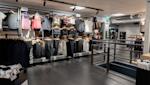 Interiör av en sportbutik med kläder på galgar i olika färger, svarta räcken och grått kakelgolv.