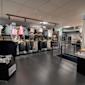 Interiör av en sportbutik med kläder på galgar i olika färger, svarta räcken och grått kakelgolv.