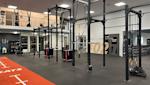 Modernt gym med svarta träningsrigg, röd löparbana och grått golv under vitt innertak med belysning.