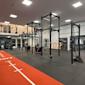 Modernt gym med svarta träningsrigg, röd löparbana och grått golv under vitt innertak med belysning.