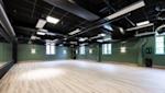 Hot studio med lyst tregulv, grønne vegger, svart tak med synlige rør og vinduer som slipper inn naturlig lys.