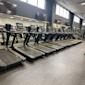 Rad av svarta löpband med digitala skärmar i ett modernt gym med stora fönster och TV-skärmar på väggen.