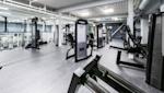 Moderne treningsstudio med svarte styrkeapparater, grått gulv og hvitt tak med synlige ventilasjonsrør.