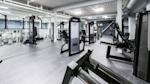 Moderne treningsstudio med svarte styrkeapparater, grått gulv og hvitt tak med synlige ventilasjonsrør.