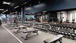 Modernt gym med hantlar i rader, träningsbänkar och utrustning under svart tak med vit belysning.
