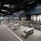 Modernt gym med hantlar i rader, träningsbänkar och utrustning under svart tak med vit belysning.