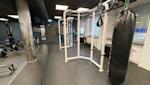Modernt gym med vit träningsram, svart boxningssäck och träningsutrustning under takbelysning med mörkt tak.