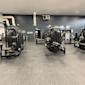 Modernt gym med svarta träningsapparater mot mörkgrå vägg, grå heltäckningsmatta och vit takpanel.